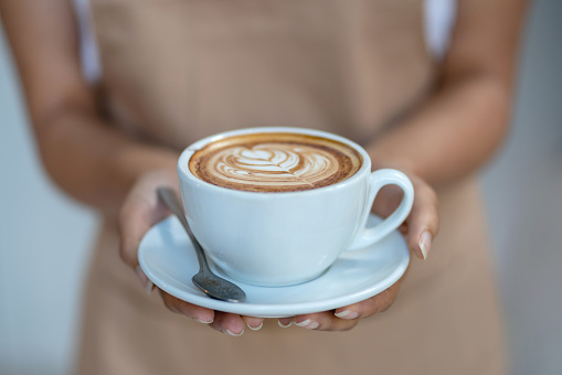 Close-up on a waitress holding a cup of coffee at a cafe â food and drink concepts
