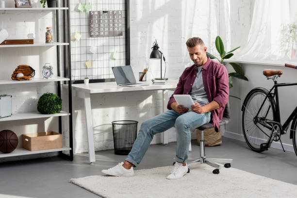 istock smiling man sitting on chair and using digital tablet at home office 1067912690