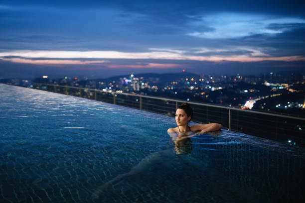 junge frau, die eine nacht schwimmen im pool in malaysia - vacations infinity pool relaxation women stock-fotos und bilder