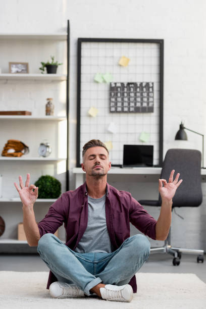 istock man sitting on floor and practicing yoga at home office 1067916484