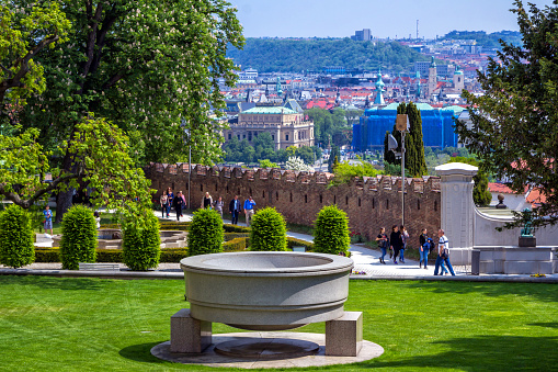 Prague/Czech Republic- May 4, 2018: cityscape of Prague from the Paradise Garden in a Royal Castle complex – view of beautiful historic buildings and tourists, walking, making photo in a park with green lawns, bushes and trees