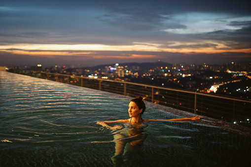 Young brunette woman relaxing in the pool, swimming on top of the building in Kuala Lumpur, Malaysia. She is having a moment to relax after work in the busy city of Kuala Lumpur, Malaysia.