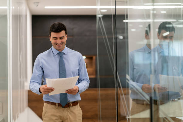 istock Portrait of young businessman walking through the office hallway while looking at documents smiling 1067920898