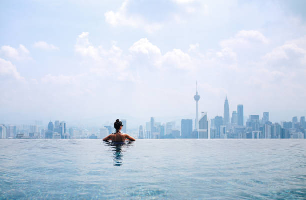 Swimming in the pool with a view Young brunette woman relaxing in the pool, swimming on top of the building in Kuala Lumpur, Malaysia. She is having a moment to relax after work in the busy city of Kuala Lumpur, Malaysia. infinity pool stock pictures, royalty-free photos & images
