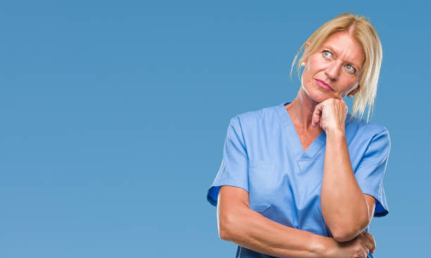 edad media mujer rubia vestida con uniforme de enfermera médico sobre aislados de fondo con la mano en la barbilla pensando en cuestión, expresión pensativa. sonriendo con cara pensativa. concepto de la duda. - portrait senior adult confusion women fotografías e imágenes de stock