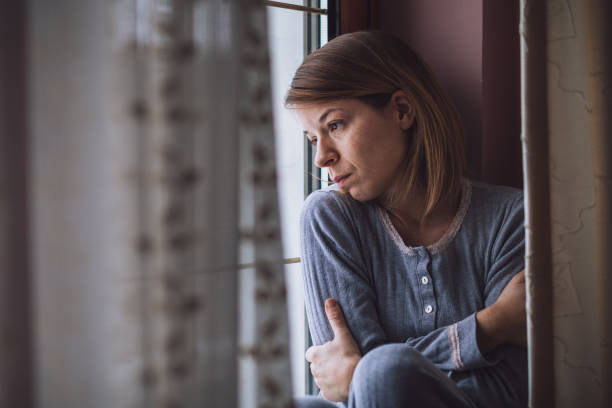 грустная женщина, сидящая у окна, глядя на улицу - mental health depression illness healthy lifestyle стоковые фото и изображения