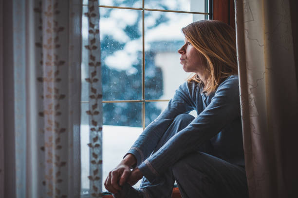 istock Sad woman sitting by the window looking outside 1067934110