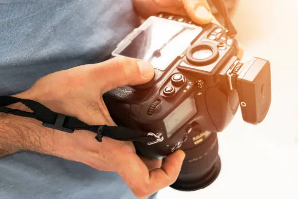 Photo of Digital single lens reflex camera in male hands. Photographer shooting hands close up. Man photographer makes photos. Male hands hold the camera close-up