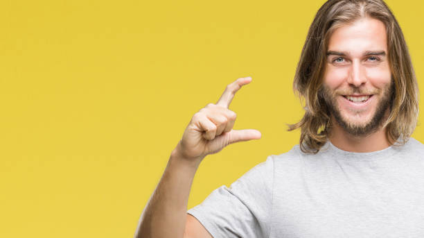 istock Young handsome man with long hair over isolated background smiling and confident gesturing with hand doing size sign with fingers while looking and the camera. Measure concept. 1067947062