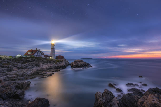 Portland Head Lighthouse lit up at night as dawn approaches Stars above the Portland Head Lighthouse at Cape Elizabeth, Maine. casco bay stock pictures, royalty-free photos & images