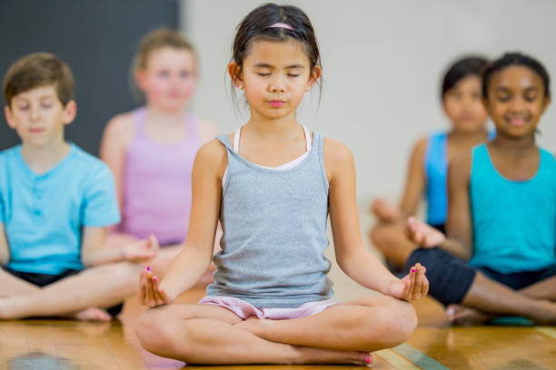 Children meditating at school A diverse group of children sit together meditating in a school gym mindfulness kids stock pictures, royalty-free photos & images