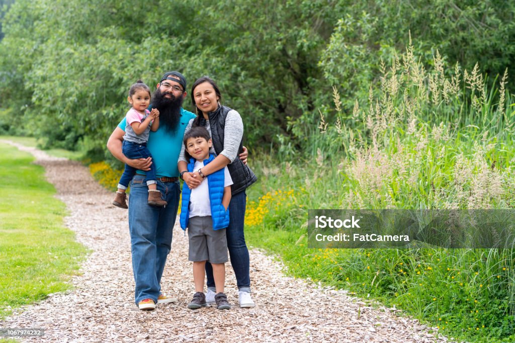 Two young kids and their parents walking out in nature An elementary-age boy and his little sister walk along a path out in nature with their mom and dad. They're paused for a moment on the path and embracing each other affectionately while they smile at the camera. Indigenous Peoples of the Americas Stock Photo