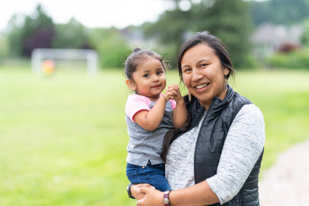 Portrait of a Native American mother and daughter outside A Native American mom holds her toddler-age daughter affectionately while they take a break from walking in the park to smile at the camera. indigenous peoples of the americas photos stock pictures, royalty-free photos & images