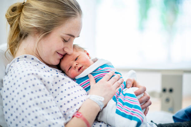 New mom holds her baby in hospital bed A caucasian mother in a hospital gown sits up in bed and holds her newborn baby to her chest new baby stock pictures, royalty-free photos & images
