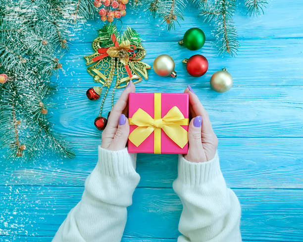 istock Christmas tree branch, female hands a gift box on a blue wooden background 1068042122