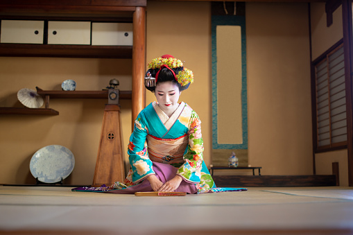 Maiko girl sitting on heels and bowing in traditional Japanese tatami room, Gion, Kyoto