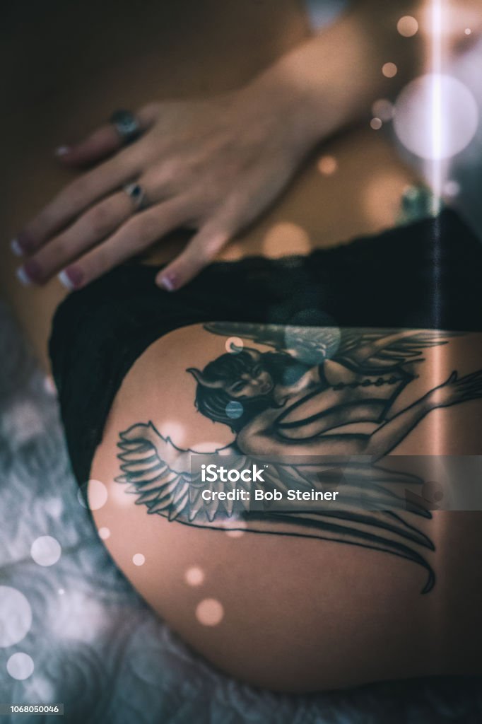 Hipster A young woman shows off a beautiful hip tattoo while lying in bed during the early morning hours of glistening light. Hip - Body Part Stock Photo