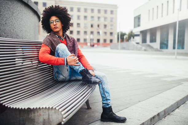 istock A handsome young Egyptian curly guy sitting on a bench dressed in a bright orange sweater and jeans. The student walks in the break between the lessons. Cute hipster guy 1068073632