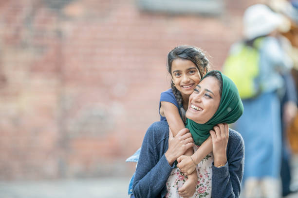 Riding On Mom's Shoulders A mother wearing a hijab is holding her daughter up on her shoulders. immigrant stock pictures, royalty-free photos & images
