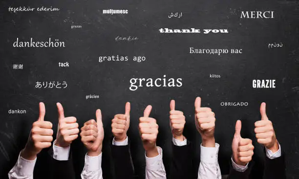 many thumbs up in front of a blackboard with the word "thank you" in many languages