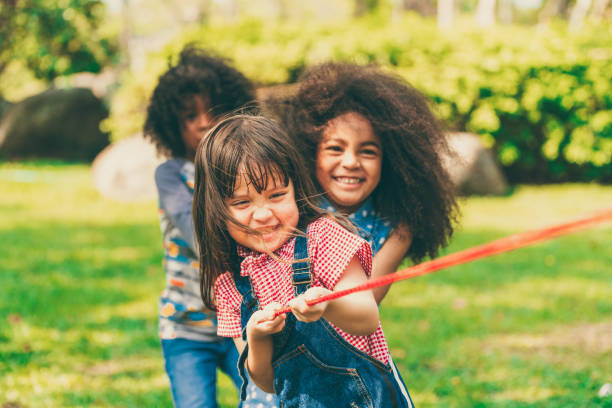Happy children playing tug of war and having fun during summer camping in the park. stock photo