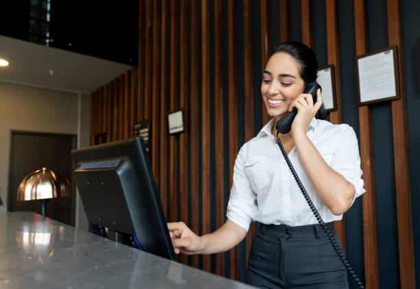 Young latin american receptionist logging a booking into the system while talking on phone smiling Young latin american receptionist logging a booking into the system while talking on phone smiling very happy hotel reception hotel service technology stock pictures, royalty-free photos & images