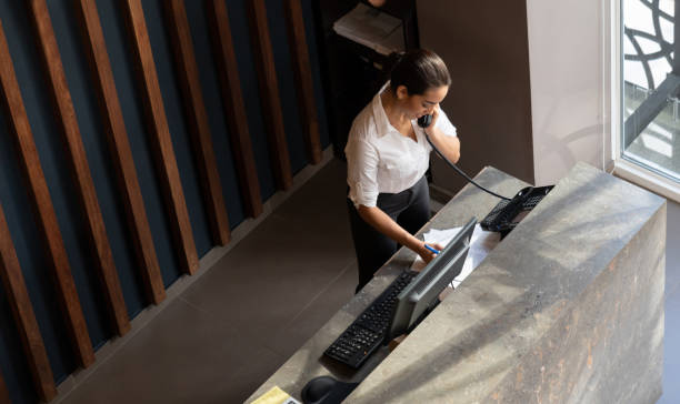Latin american hotel receptionist taking a phonecall Latin american hotel receptionist taking a phonecall writing something down on document concierge photos stock pictures, royalty-free photos & images