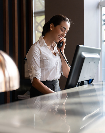 Portrait of beautiful young receptionist answering a phonecall at the front desk of hotel smiling