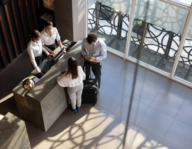 Black manager and recepcionist checking in a couple and man looking at his smartphone Black manager and recepcionist checking in a couple and man looking at his smartphone at the hotel hotel reception hotel service technology stock pictures, royalty-free photos & images