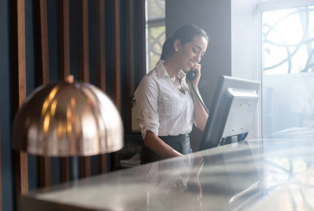 Beautiful friendly hotel receptionist answering a call from a guest Beautiful friendly hotel receptionist answering a call from a guest smiling very happy concierge photos stock pictures, royalty-free photos & images