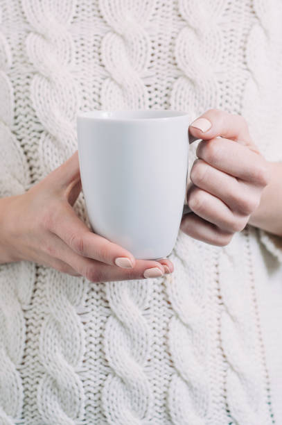 istock A woman in a white sweater holding a white mug in her hands. Template for text or design 1068231002