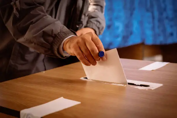 Color image of a person casting a ballot at a polling station, during elections.