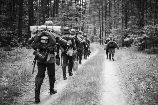 re-enactors disfrazados de soldados de infantería alemana en la segunda guerra mundial marchando a pie por camino de bosque en día de verano. foto en blanco y negro colores - ii fotografías e imágenes de stock