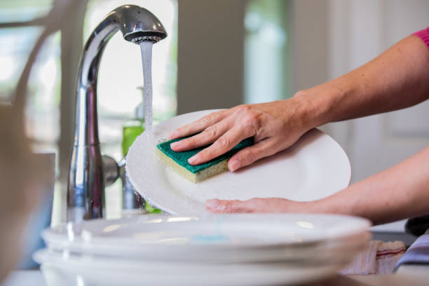 istock Woman using sponge to scrub plate while washing dishes 1068248476