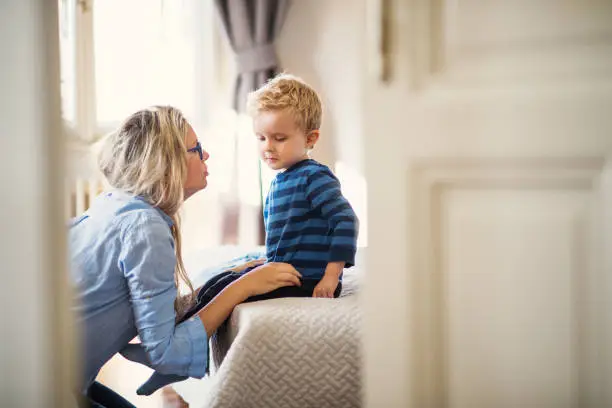 Photo of A young mother talking to her toddler son inside in a bedroom.