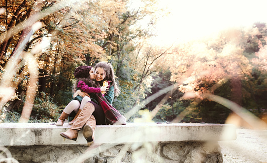 A young mother with a toddler daughter hugging and kissing in forest in autumn nature.