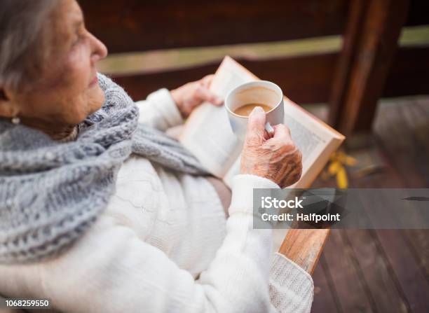 An Elderly Woman Reading Book Outdoors On A Terrace On A Sunny Day In Autumn Stock Photo - Download Image Now