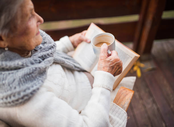 uma mulher idosa lendo livro ao ar livre no terraço em um dia ensolarado no outono. - falling senior adult people one person - fotografias e filmes do acervo
