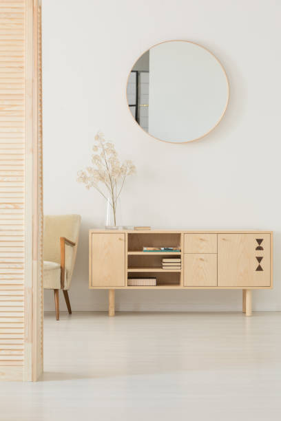 espejo redondo colgado en la pared blanca en la foto real del luminoso salón interior con armario de madera con los libros y de la planta en florero de vidrio - round mirror fotografías e imágenes de stock