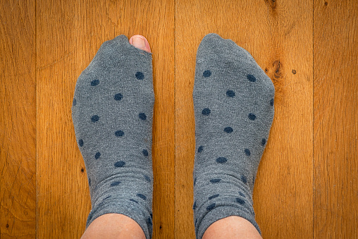 A pair of socks. A sock with a hole. the big toe shows through a hole in the sock.