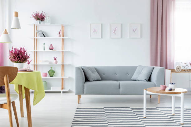 istock Trendy interior design with comfortable scandinavian couch, wooden coffee table, striped rug and graphics on the floor, real photo 1068275536