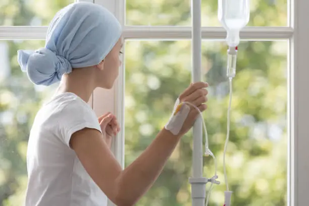 Sick child with drip wearing blue headscarf during treatment in the hospital