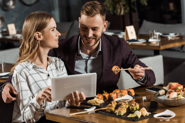 istock Beautiful young adult couple using digital tablet while having dinner in restaurant 1068293226