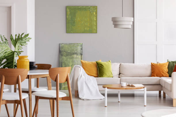 istock Wooden chairs at table in grey flat interior with pillows on corner couch near green posters. Real photo 1068302818
