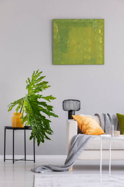istock Plant on table next to settee with lamp and blanket in grey loft interior with green poster. Real photo 1068302826