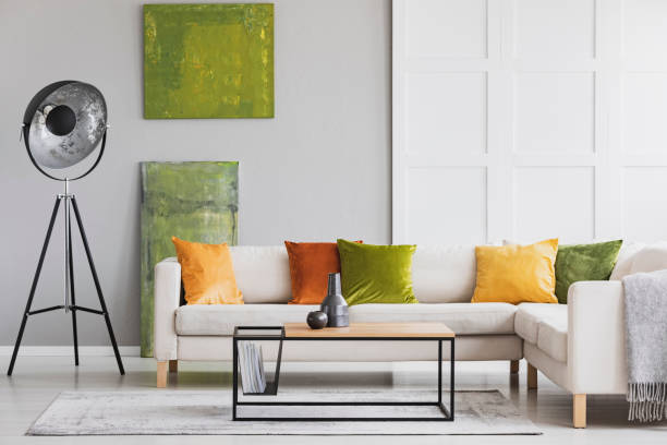 istock Pillows on corner sofa next to lamp in living room interior with green posters and table. Real photo 1068302828
