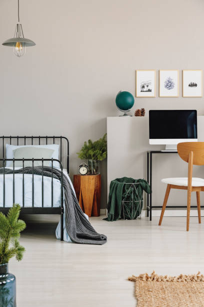 istock Single metal bed with blue bedding next to wooden nightstand and desk with computer, real photo with copy space on the empty grey wall 1068306464