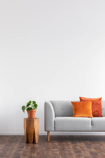 istock Orange cushions on grey settee next to plant on wooden table in grey flat interior. Real photo 1068309838