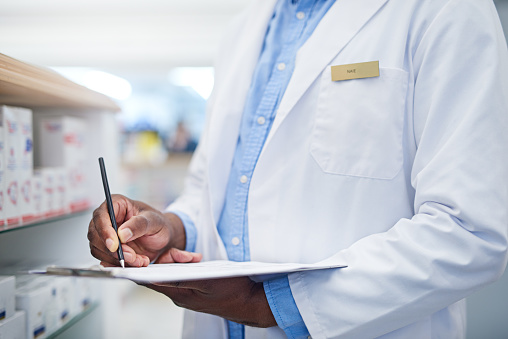 Closeup shot of an unrecognizable pharmacist writing on a clipboard in a chemist