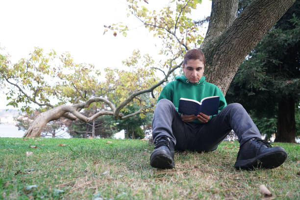 istock Young man reading book in park 1068326012